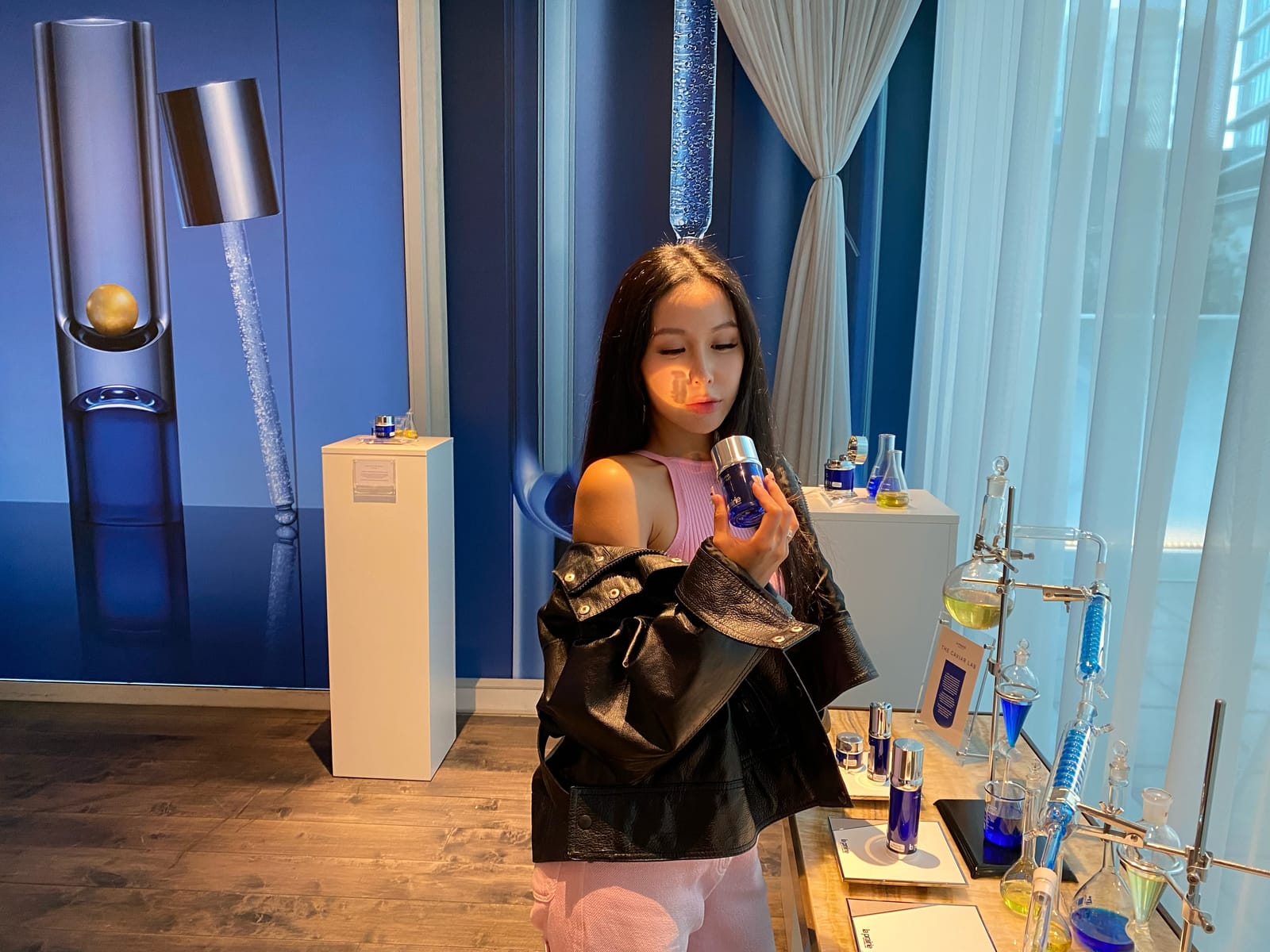 Chelsea holding a skincare jar beside a blue product display